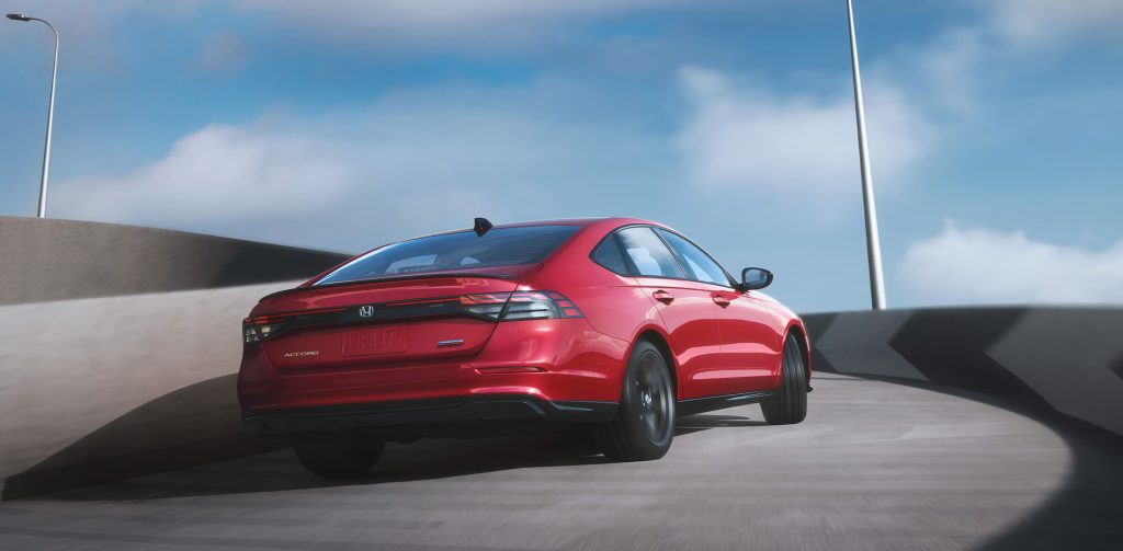 A red 2025 Honda Accord cruising along a winding road beneath a clear, bright sky.