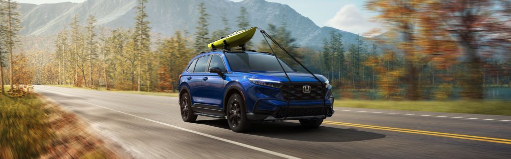 2026 Honda CR-V Blue driving on scenic road with kayak on roof.