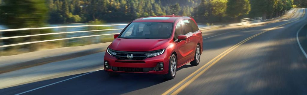 2026 Red Honda Odyssey driving on a scenic road.