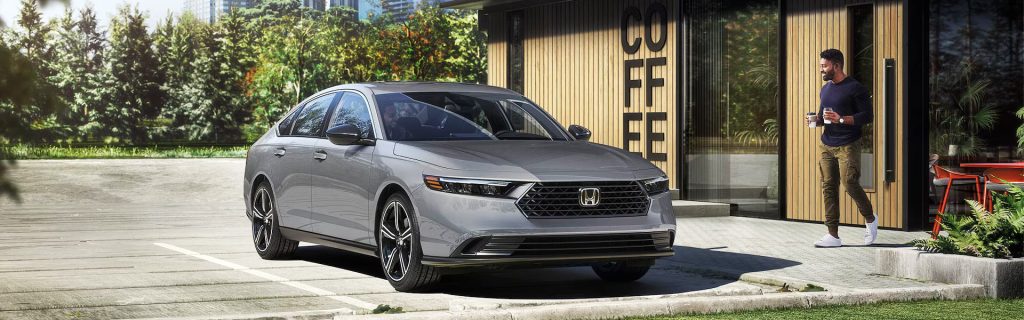 Silver 2026 Honda Accord sedan parked outside a modern café, highlighting its updated styling, advanced technology, and efficient daily-driver design.