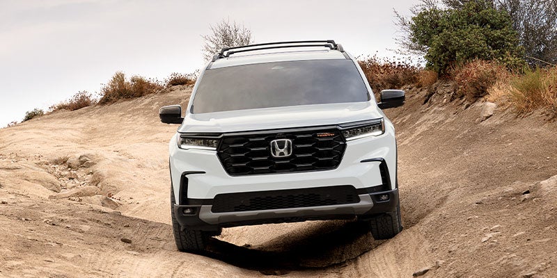 White Honda Pilot SUV driving off-road through a rugged dirt trail.