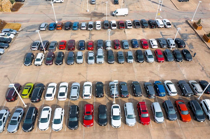 Aerial view of a large car dealership lot filled with rows of parked used vehicles.