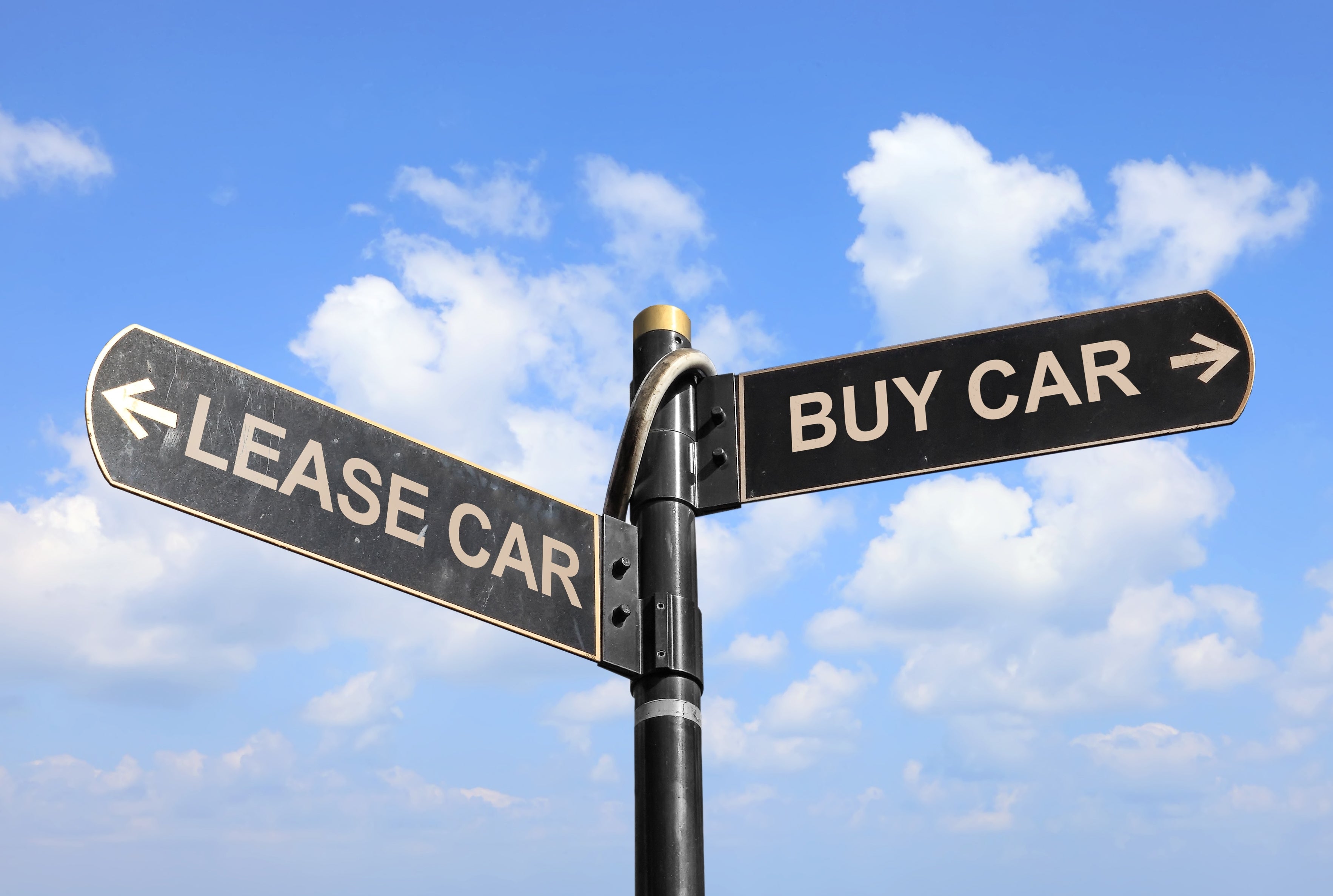 Direction sign showing options to buy or lease a car against a blue sky background.