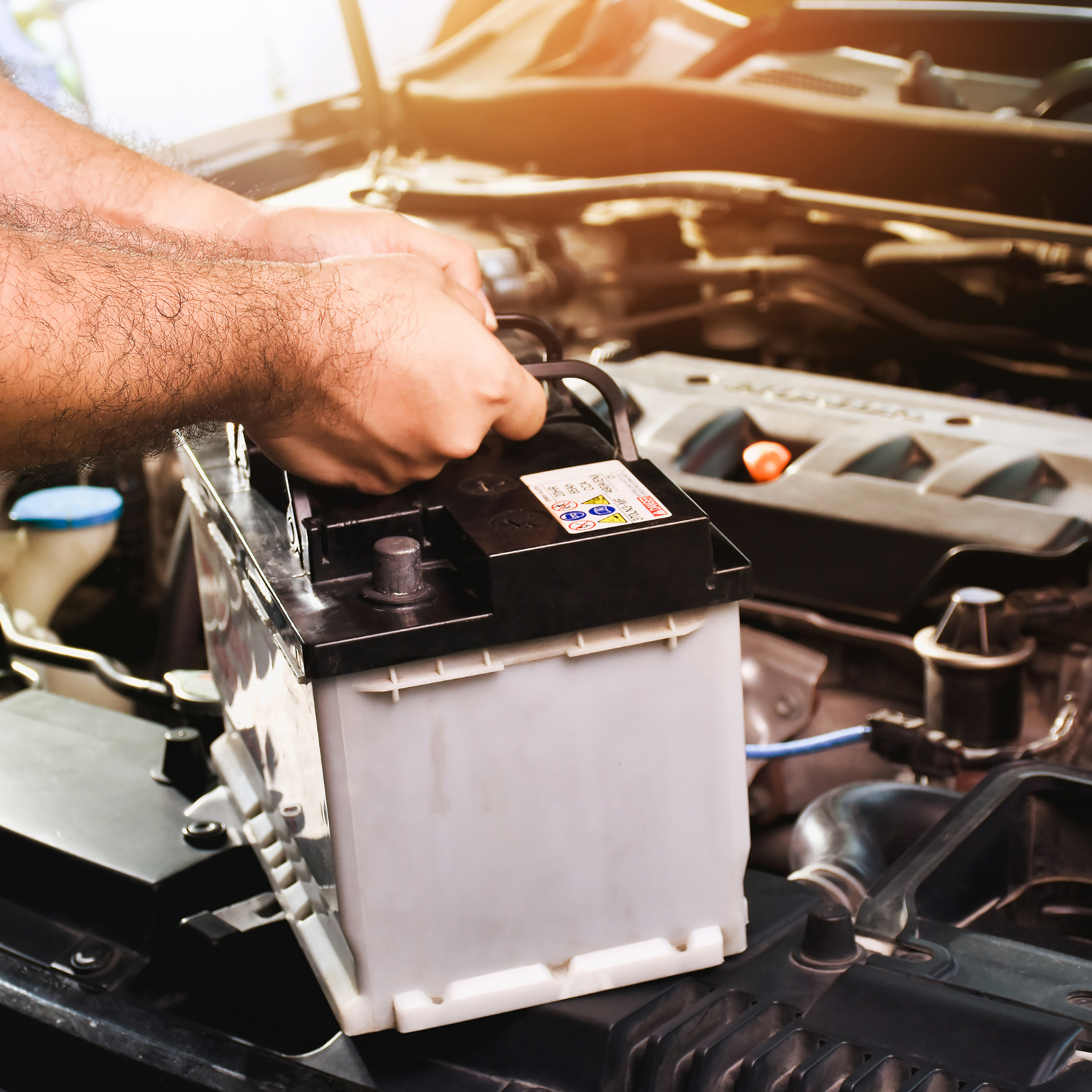 Automotive technician installing or inspecting a car battery under the vehicle hood.